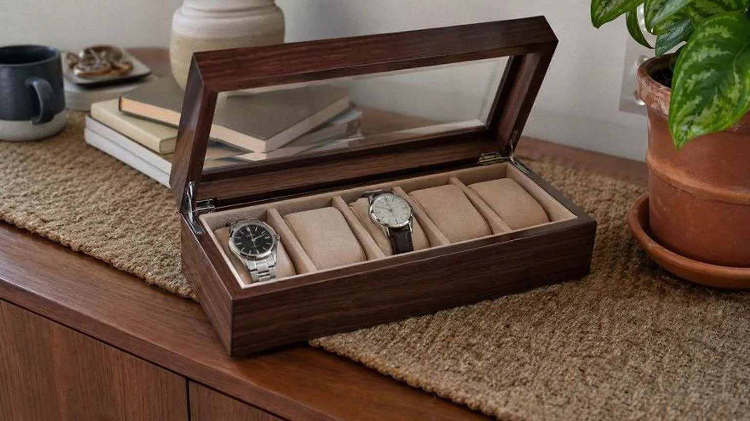 Caja de relojes de madera de nogal con tapa de cristal abierta y relojes automáticos sobre cojines beis